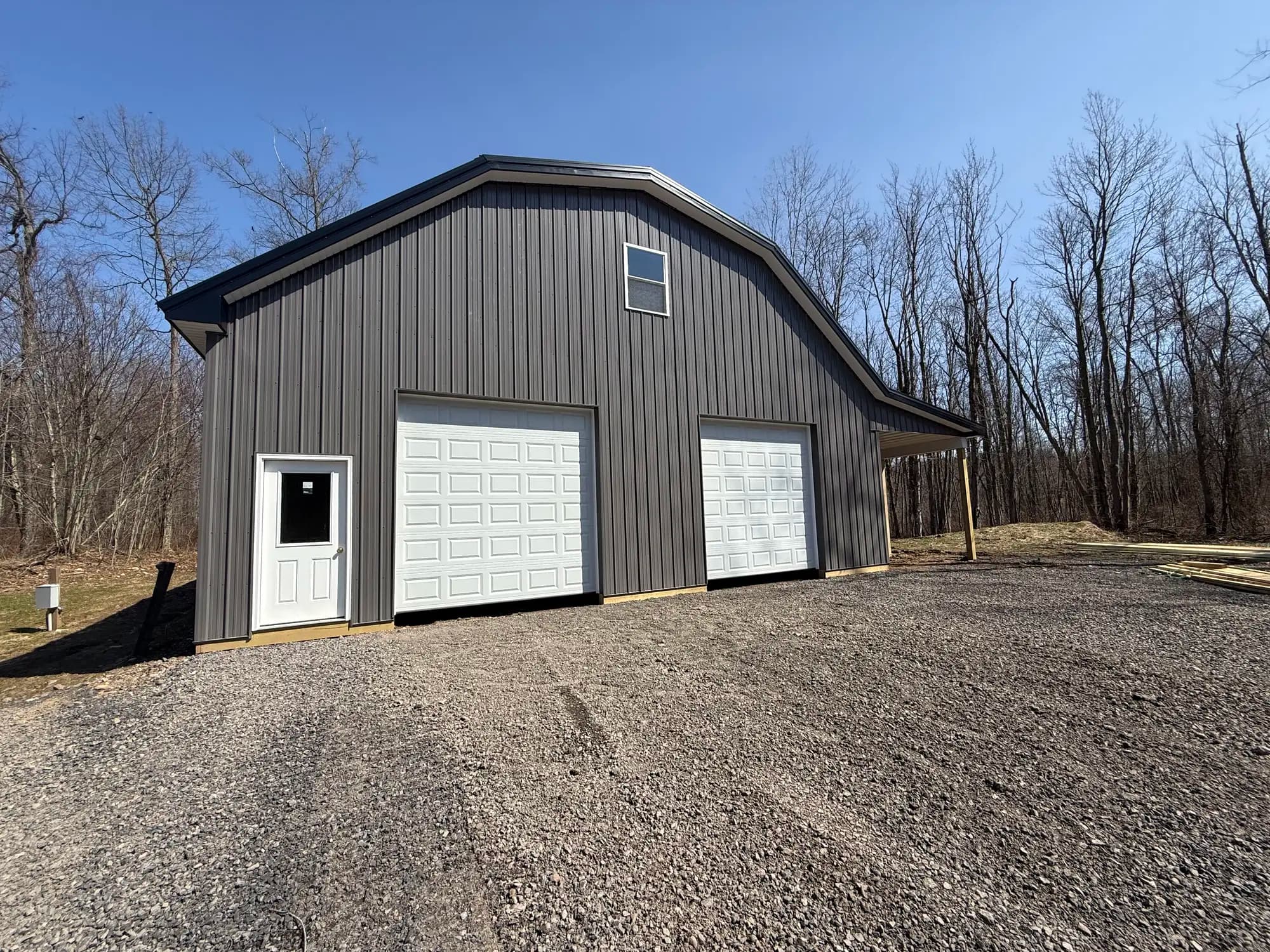 Dark charcoal barndominium with gambrel roof and white garage doors